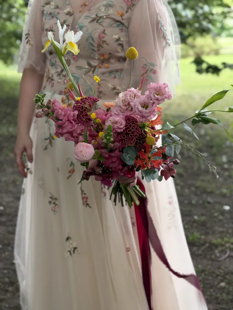 Panna młoda w haftowanej sukni z bukietem w różach, fuksji i pomarańczach